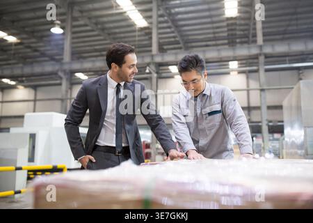 Hispanic businessman talking to Chinese male engineer standing near boxes in factory Stock Photo