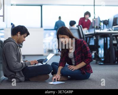 Mixed race man and female workmate working together sitting on floor in office Stock Photo