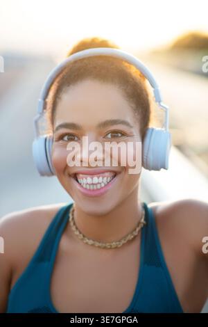 Smiling Mixed race woman in headphones standing outdoors on sunny day Stock Photo