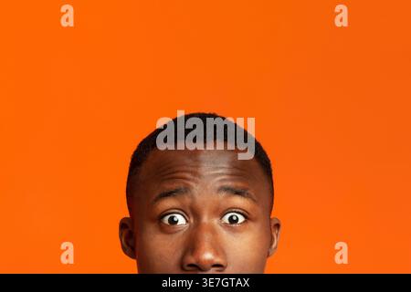 Head of Black man with surprised eyes against orange background in studio Stock Photo