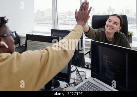 Smiling Black man and Mixed race woman doing high five working together sitting at table in office Stock Photo