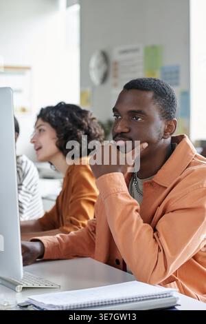 Black male teenager student working on computer with group of female colleagues while sitting at table in classroom Stock Photo