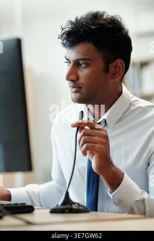 Indian male manager sitting at table working on surveillance computer in security room Stock Photo