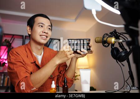 Asian man making video for blog demonstrating new eyeshadow palette at home Stock Photo