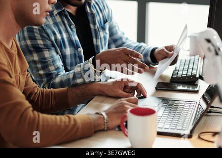 Indian male programmer discussing new program with male colleague while sitting at desk in office Stock Photo