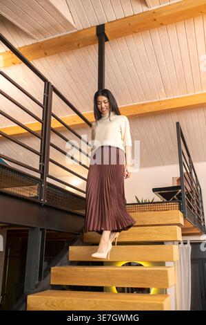 Smiling Hispanic woman walking down on stairs at home during daytime Stock Photo