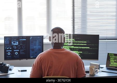 Back view of Black male programmer examining codes on computer while sitting at table in office Stock Photo