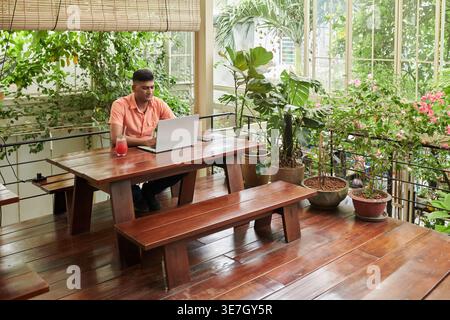 Indian male entrepreneur working on laptop sitting at table with drinks in cafe Stock Photo