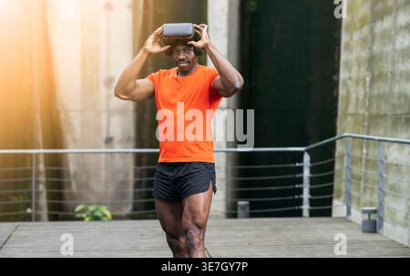 Black man wearing VR goggles experiencing virtual reality while standing in city park during daytime Stock Photo