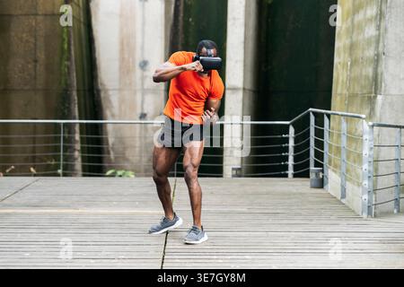 Black man wearing VR goggles training boxing punches while standing in city park during daytime Stock Photo