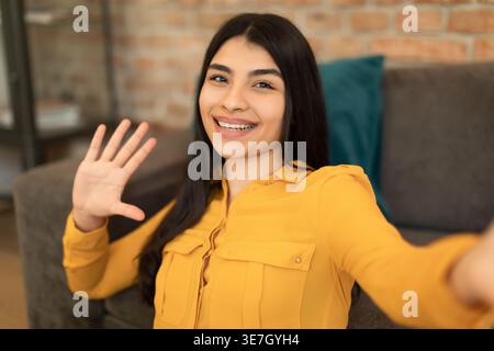 Smiling Middle Eastern woman showing five fingers while sitting on floor near sofa in living room at home Stock Photo