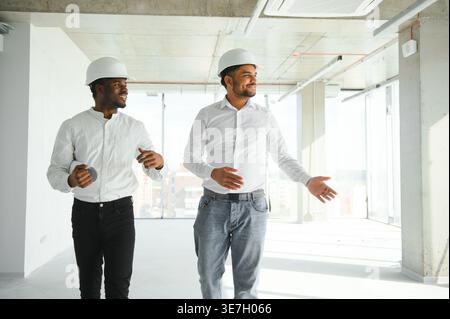 Diverse group of male engineers wearing hard hats walking together and doing inspection on construction site Stock Photo