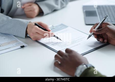 Closeup of Black man holding resume asked by caucasian manager regarding previous experiences sitting at table in office during job interview Stock Photo