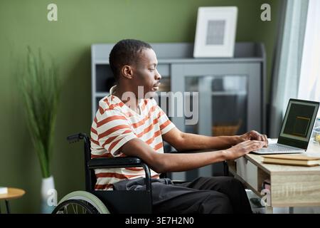 Disabled Black man in wheelchair using laptop working from home Stock Photo