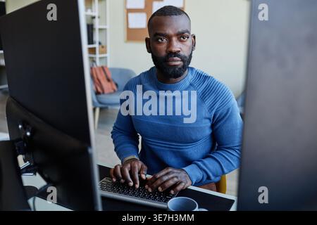 Black male programmer with beard typing codes on computer while sitting at table in office Stock Photo