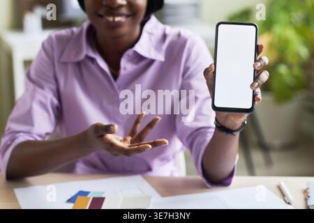 Black female designer with braids showing smartphone while sitting at table in office Stock Photo