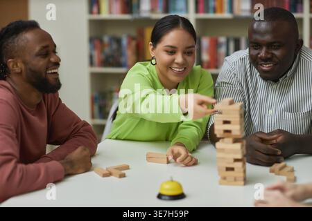 Diverse group of friends playing jenga while sitting together at table in college library Stock Photo