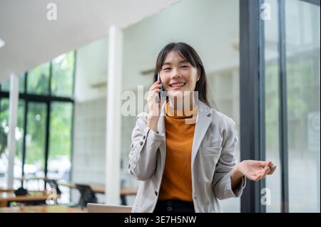 Thai woman having phone conversation standing in office during daytime Stock Photo