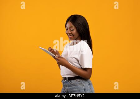 Black woman in white t-shirt using tablet standing against yellow background in studio Stock Photo