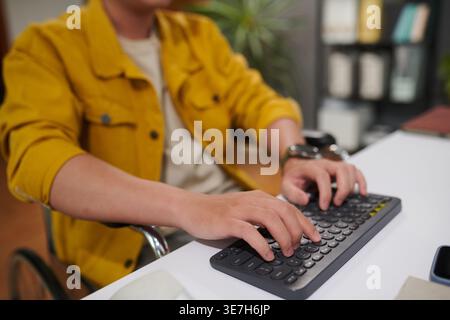 Asian man with disability working on computer sitting in wheelchair in office Stock Photo