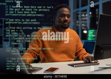 Black male programmer examining computer codes sitting at table working late at night in office Stock Photo