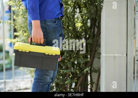 Cropped image of Asian repairman with toolbox standing on porch of clients house Stock Photo