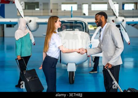 Smiling African American businessman shaking hands with female pilot near private jet in hangar Stock Photo