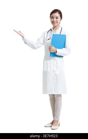 Smiling Chinese female doctor holding clipboard doing welcome gesture standing against white background in studio Stock Photo