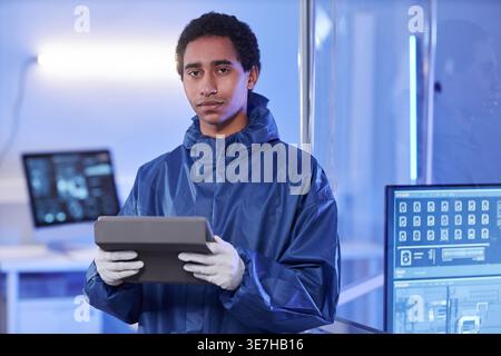 Mixed-race male scientist wearing protective suit and gloves holding tablet while standing in laboratory Stock Photo