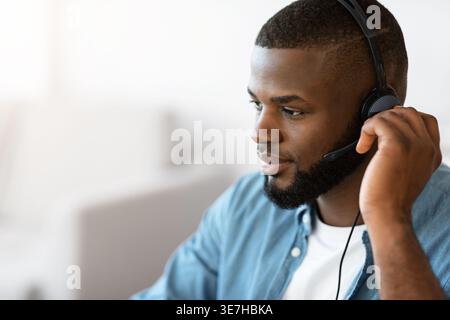 Smiling bearded Black male freelancer wearing headset having videocall while sitting at table in home office Stock Photo