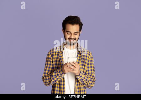 Indian man using smartphone standing against purple background in studio Stock Photo