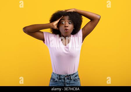 No Way. Portrait of very surprised black lady looking at camera and grabbing her head, being shocked by cool offer, standing over yellow background, s Stock Photo