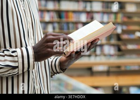 Black man wearing stripe long sleeves reading book while standing in library Stock Photo