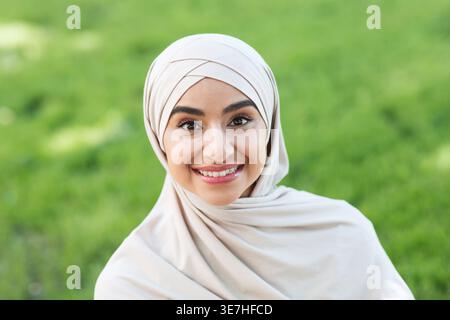 Portrait image of smiling Indian Muslim woman wearing hijab sitting on plaid blanket in park during daytime Stock Photo