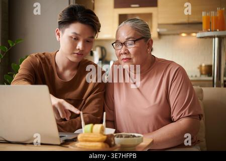 Asian grandmother wearing eyeglasses learning how to setup wifi router with her grandson while sitting on sofa at home Stock Photo