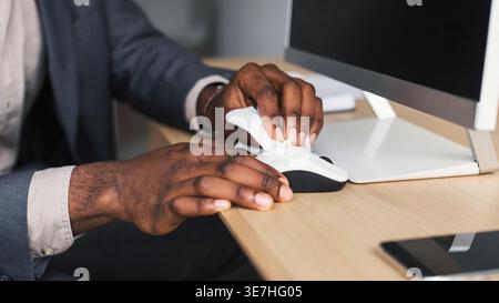 Black businessman wiping computer mouse using napkin sitting at table in office Stock Photo