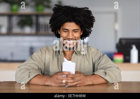 Black male with afro using smartphone sitting at table in cafe Stock Photo