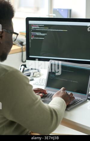 Black male programmer writing codes on laptop while sitting at table with coffee in office Stock Photo
