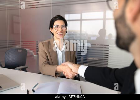 Businesswoman shaking hands with male client during formal office meeting Stock Photo