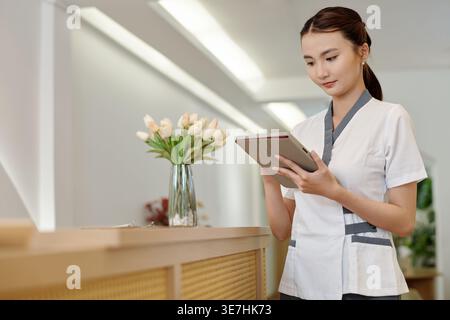 Asian female receptionist standing and checking schedule using tablet in spa salon Stock Photo
