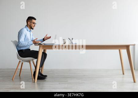Middle Eastern man wearing eyeglasses having online meeting sitting at table in office Stock Photo