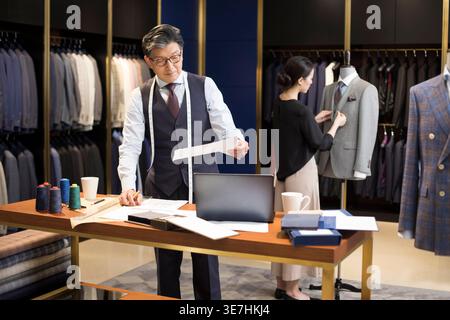 Middle-aged Chinese male and female fashion designer working together on their design in fashion boutique Stock Photo