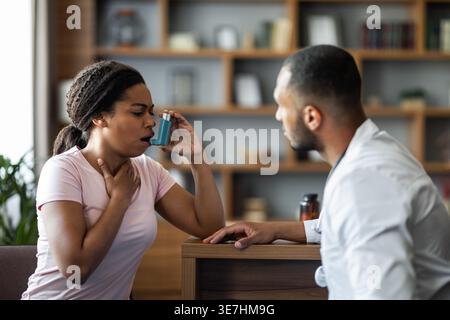 Black female patient touching neck using nebulizer sitting in front of male doctor during consultation in clinic Stock Photo