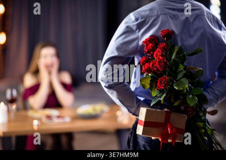 Black man holding bouquet while standing near table with his caucasian girlfriend during dinner date in restaurant Stock Photo
