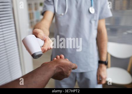 Hand of Black man getting his body temperature checked using infrared thermometer by male nurse in clinic Stock Photo