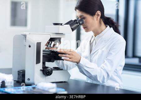 Chinese female scientist looking through microscope while working in laboratory Stock Photo
