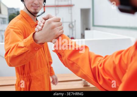 Asian and mixed race male construction workers shaking hands while standing in construction site Stock Photo