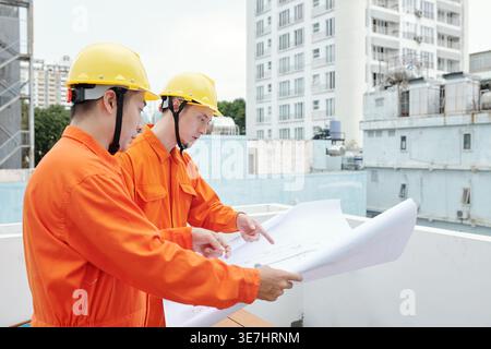 Asian and mixed race male construction workers discussing plan of structure while standing in construction site Stock Photo