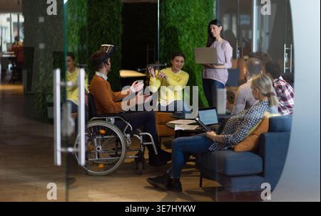 Diverse group of business people with disabled caucasian businessman using VR goggles and drone assistance simulation while having a meeting in the... Stock Photo