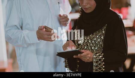 Middle Eastern businessman and business woman holding tablet and smLifestylephone while standing and discussing work in the office Stock Photo